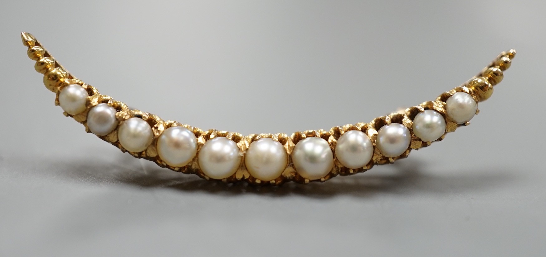 An early 20th century yellow metal and graduated cultured pearl set crescent brooch, 40mm, gross weight 3.7 grams.